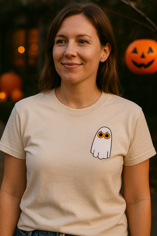 Woman wearing a beige t-shirt with a ghost wearing pumpkin glasses design in front of Halloween-themed decorations.